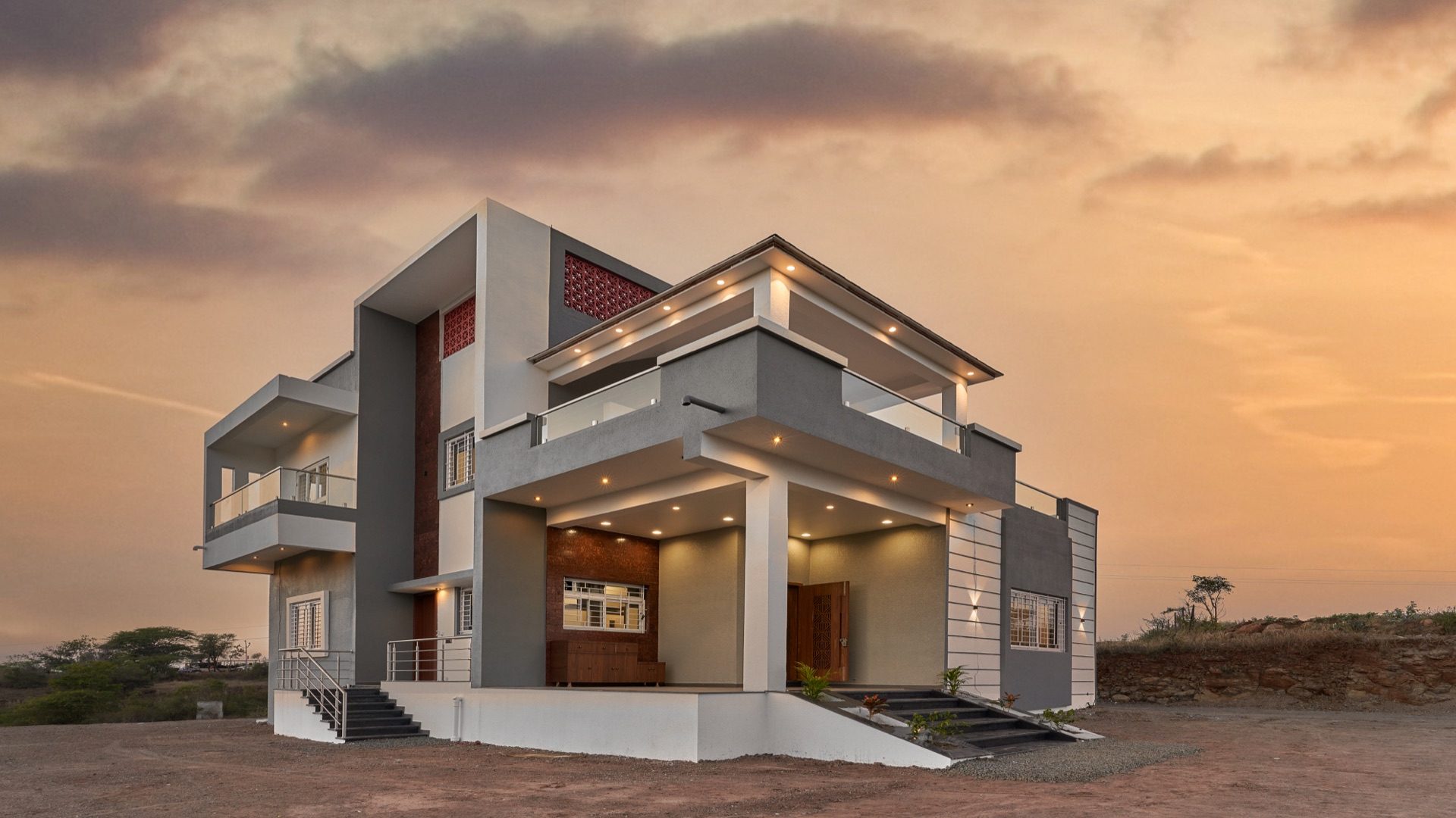 Layered grey-and-white contemporary bungalow lit up against a sunset sky — Kondhanpuri